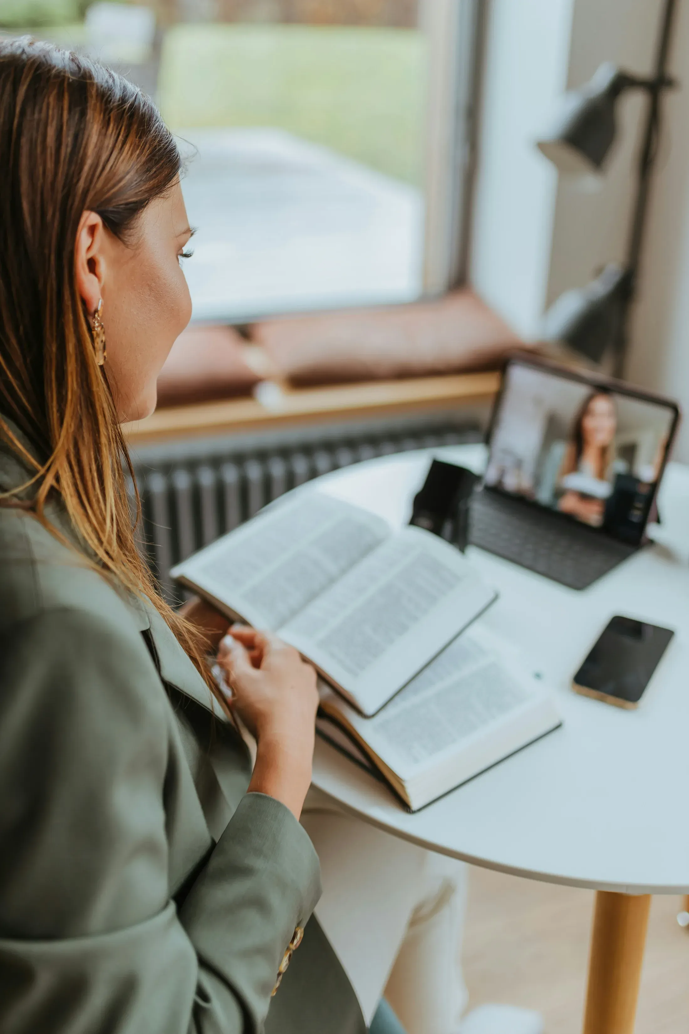 A woman at a desk with an open book, talking with someone over a video call