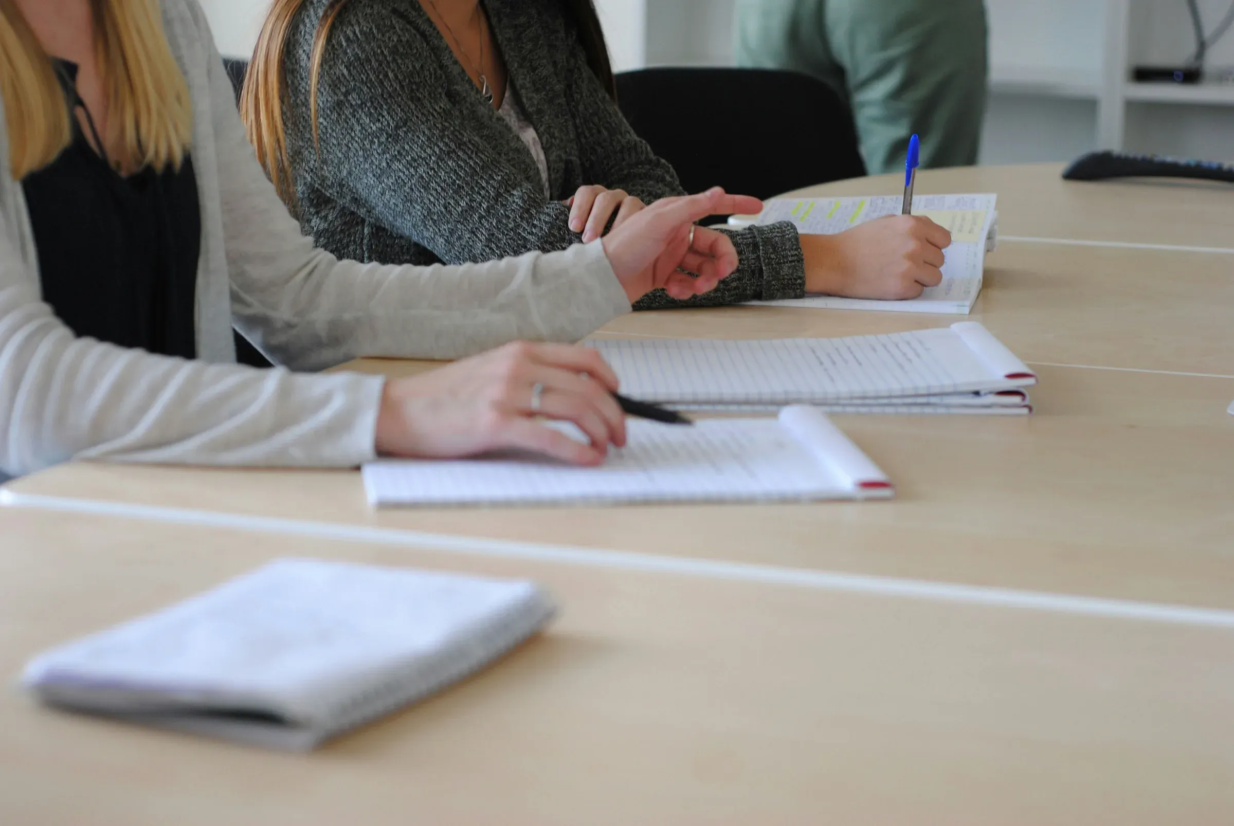 Hands taking notes in notebooks at a shared table