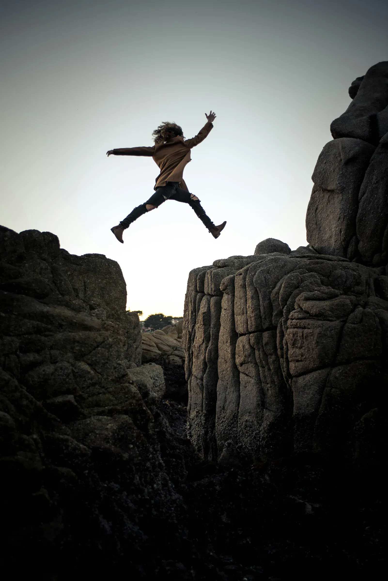 A young person leaping between rocks against an open sky