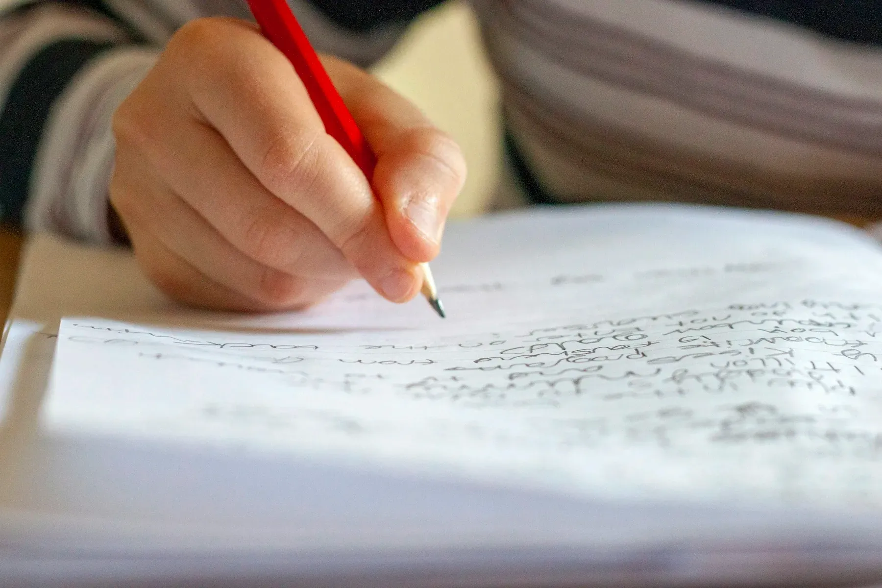 A child's hand gripping a pencil over a page filled with small, closely written handwriting