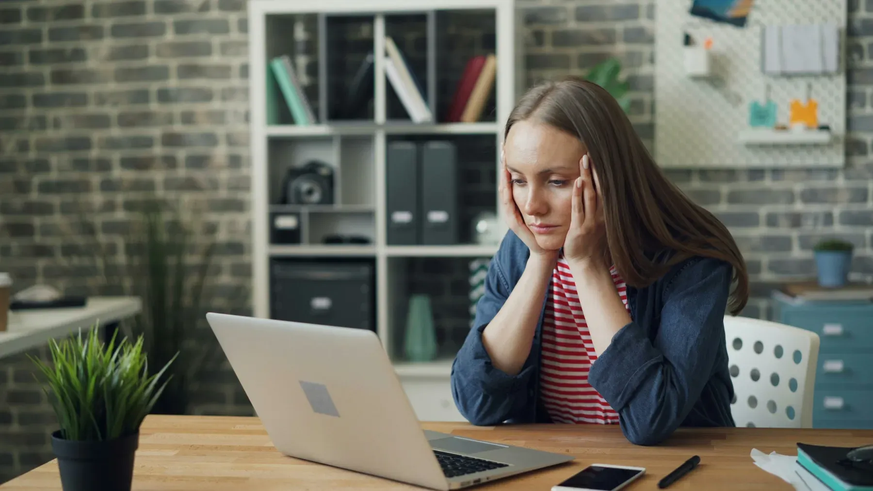A parent sitting at a laptop with her head in her hands