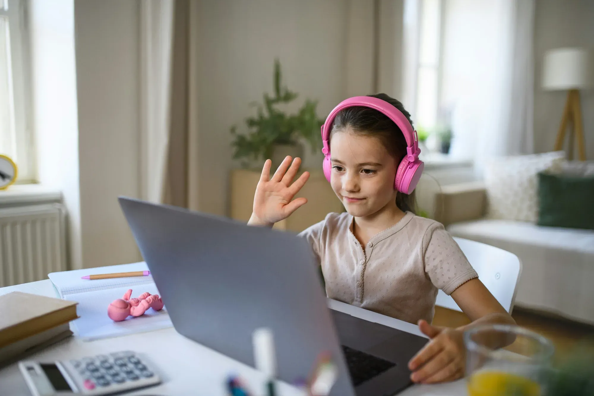 A student in headphones waving to the screen at the start of an online session