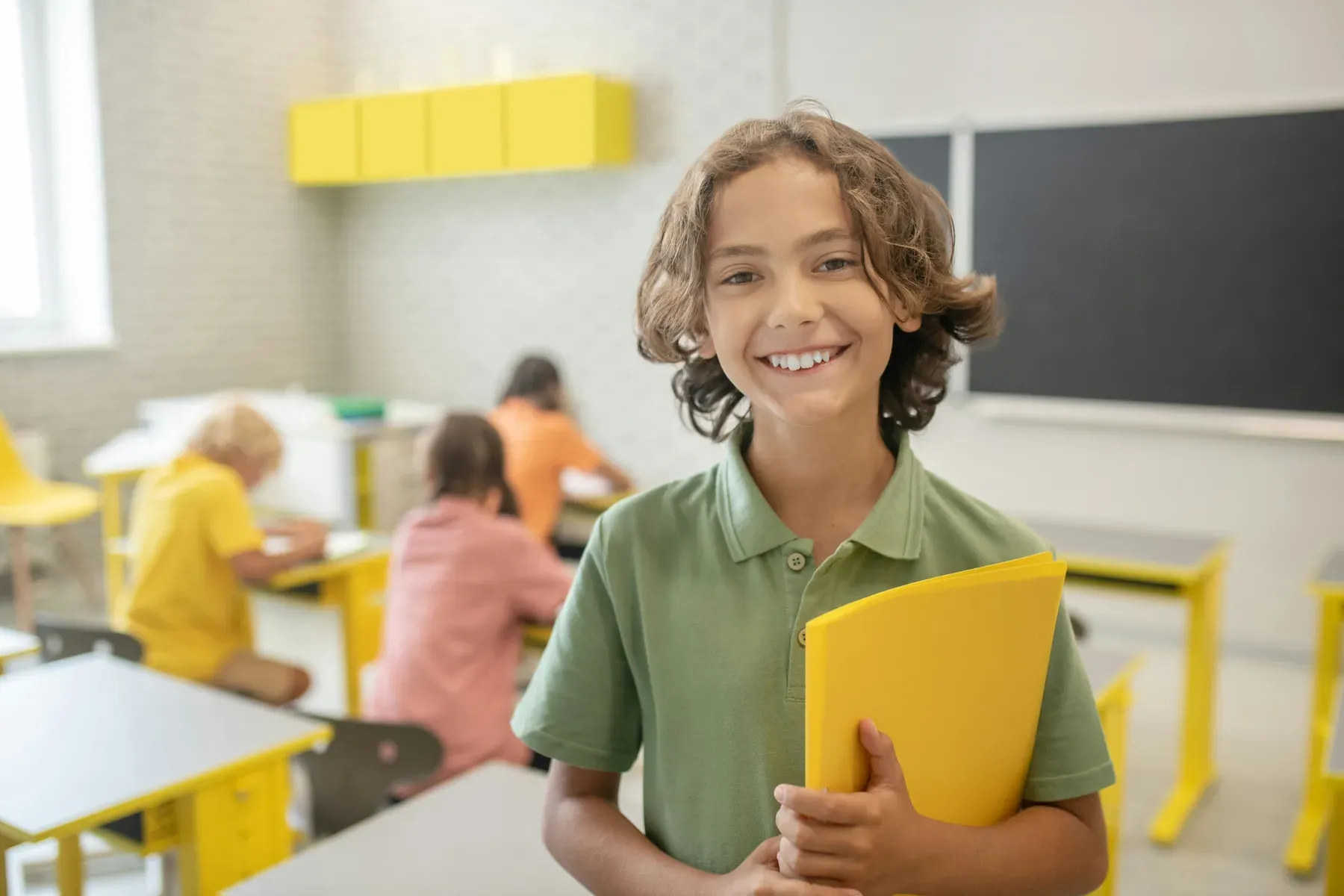 A smiling student holding a folder in a bright classroom