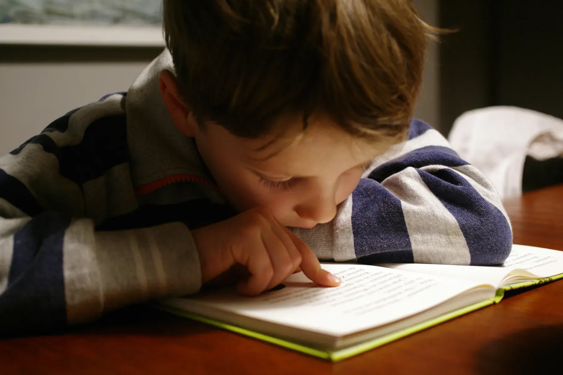 A young student reading a book, tracking the line with a finger